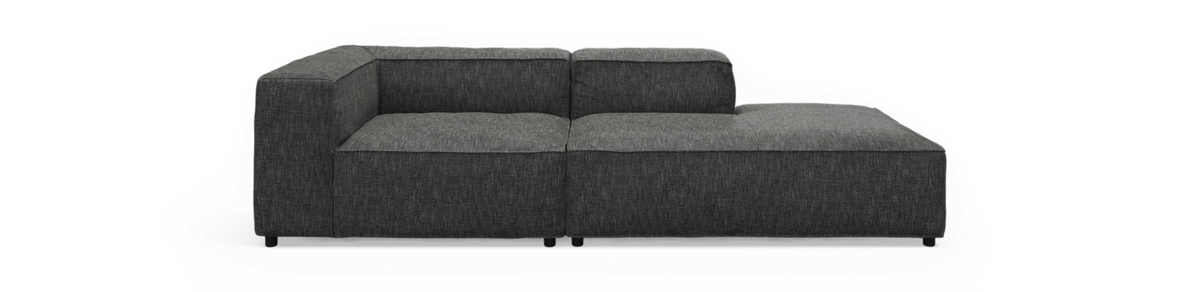 Mørkegrå L‑formet modulsofa med chaiselong til højre, frilagt mod sort baggrund, set forfra.
