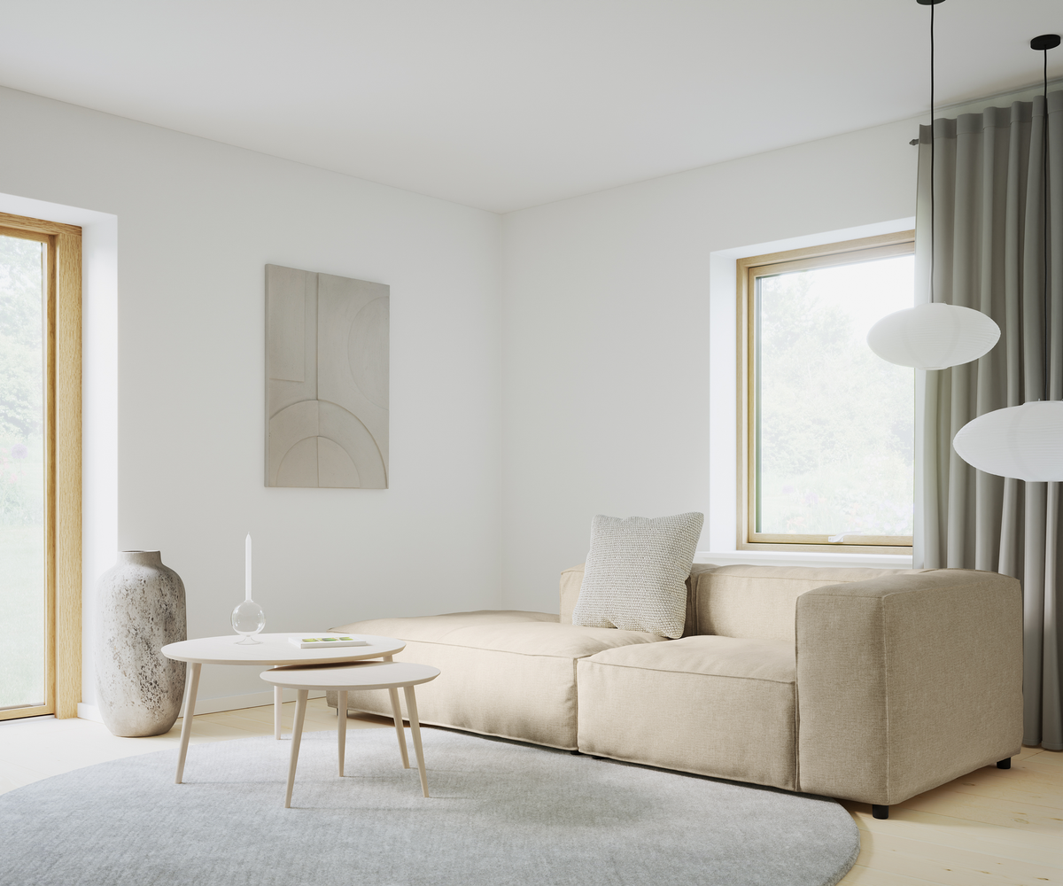 Lys stue med beige modulsofa, runde sofaborde og gråt rundt tæppe, papirpendler og store vinduer med gardiner.