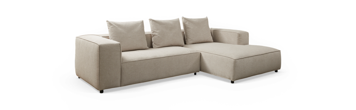 Beige hjørnesofa med chaiselong til højre og tre løse ryghynder, fritlagt mod sort baggrund.