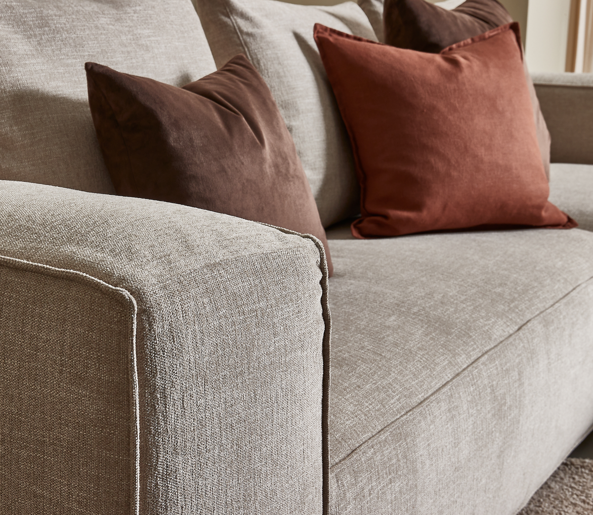 Nærbillede af beige stofsofa med brune og rustfarvede fløjlspuder.