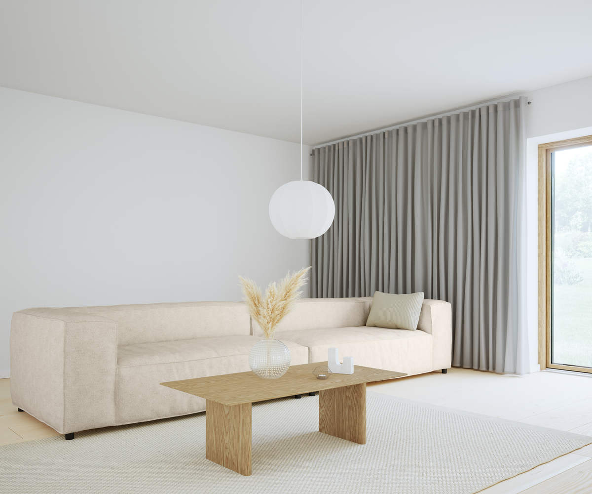 Lys skandinavisk stue med beige sofa, træbord med glasvase og pampasgræs, rund hvid pendellampe og grå gardiner ved stort vindue.