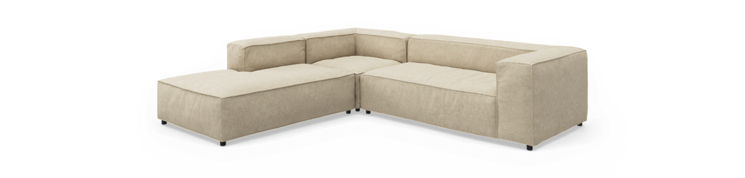 Beige L-formet modulsofa med lav ryg og brede armlæn, frilagt på hvid baggrund.