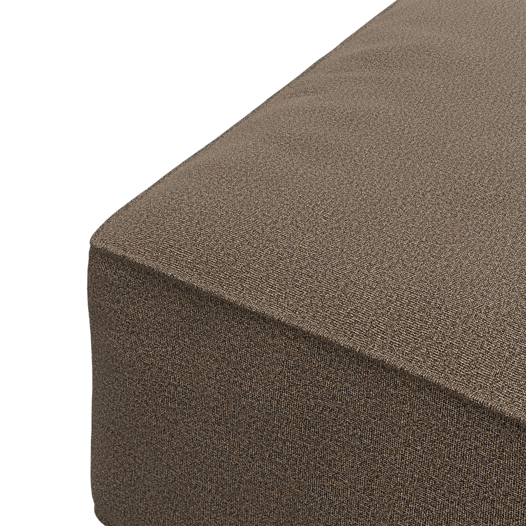 Nærbillede af brun stofbetrukket pouf/ottoman i skrå vinkel, frilagt.