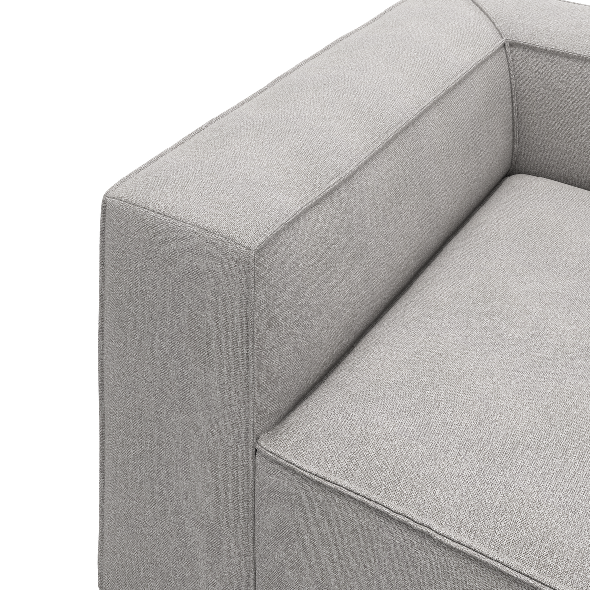 Nærbillede af en lysegrå stofsofa med bredt armlæn og boxet sæde i minimalistisk design.