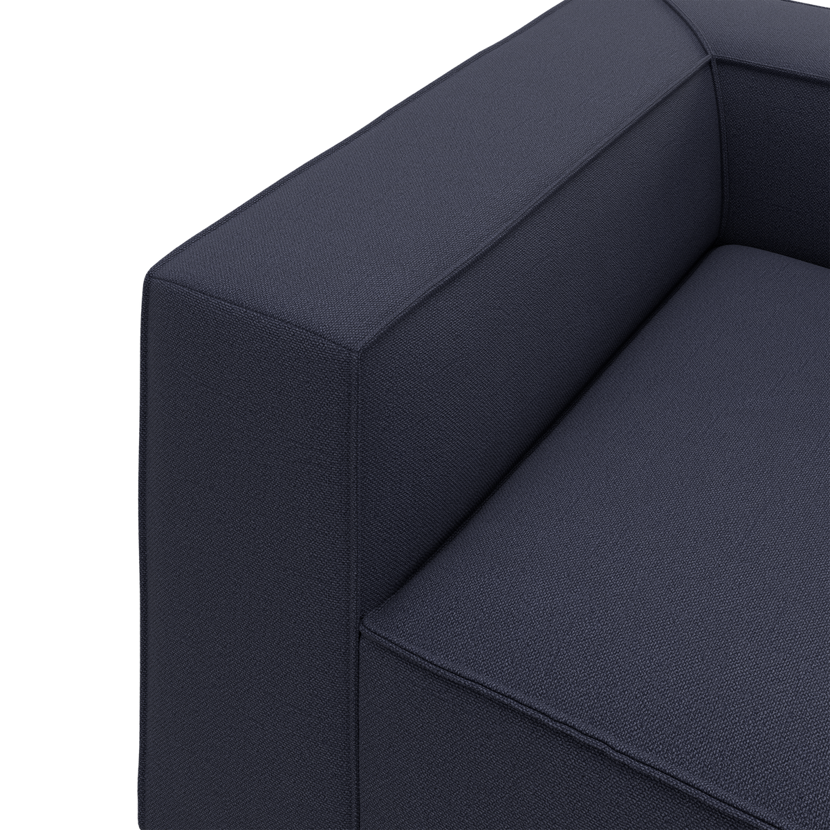 Nærbillede af mørkeblå stofsofa med armstøtte og sæde i minimalistisk, boxet design.