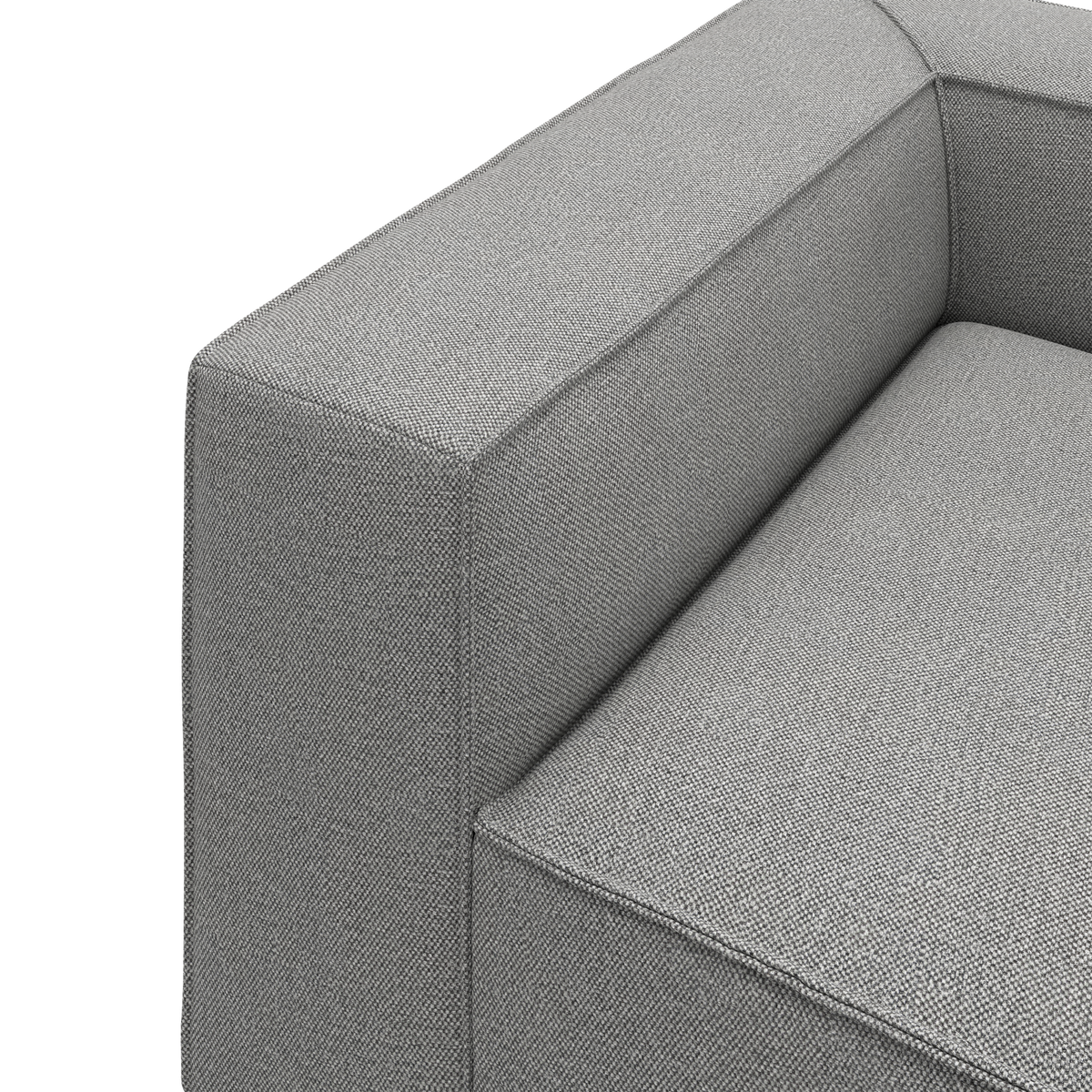 Nærbillede af gråt stofbetrukket sofa-armlæn og sædepude i boxet, moderne design på hvid baggrund.