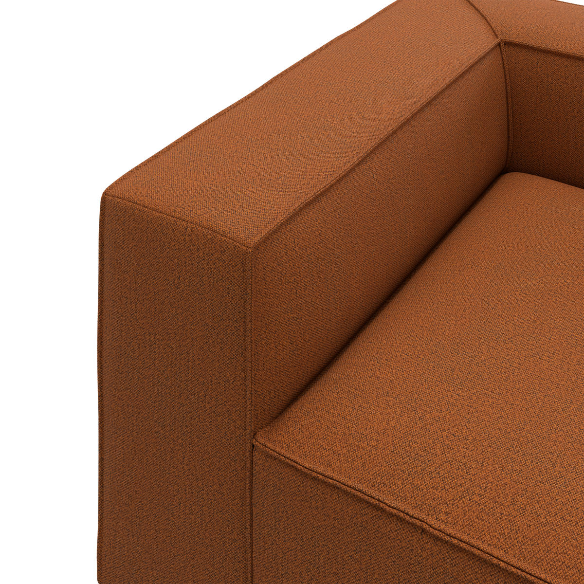Nærbillede af en rustfarvet stofsofa med kantet armlæn og sæde i moderne, boxet design.
