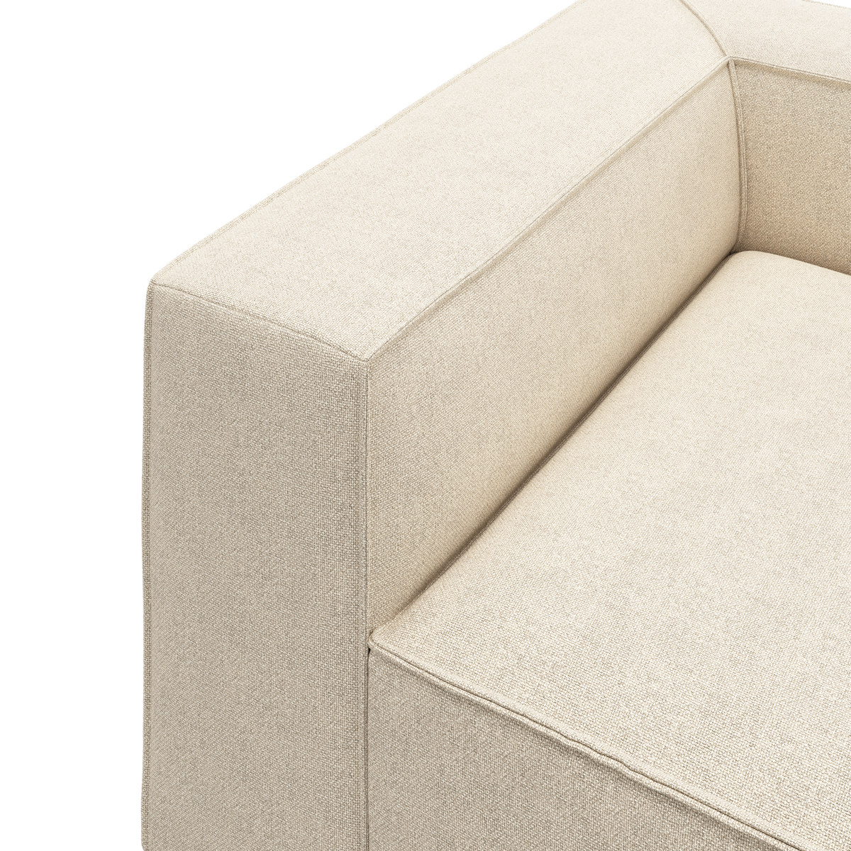 Nærbillede af en beige stofsofa med boxet armlæn og sæde i minimalistisk stil på hvid baggrund.