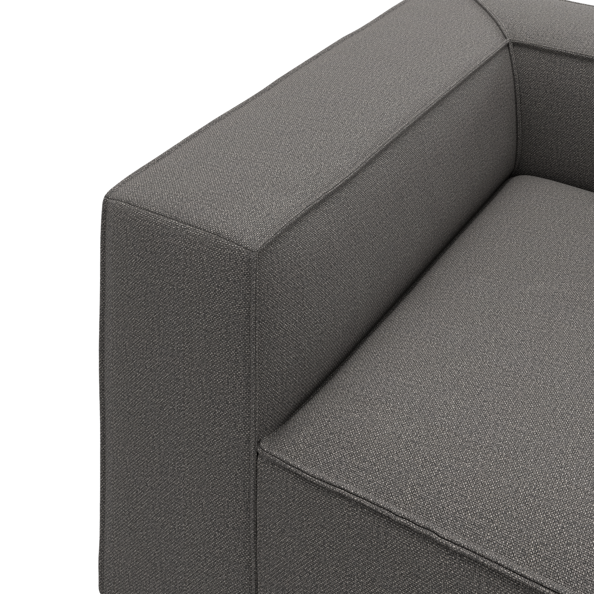 Nærbillede af en grå stofsofa med bredt, kvadratisk armlæn og fast sæde i moderne, minimalistisk design.