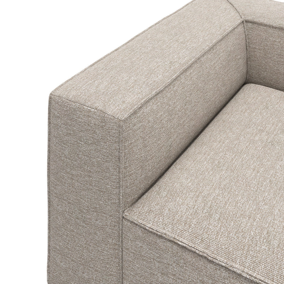 Nærbillede af beige stofsofa med kantet armlæn og sæde i studiemiljø.