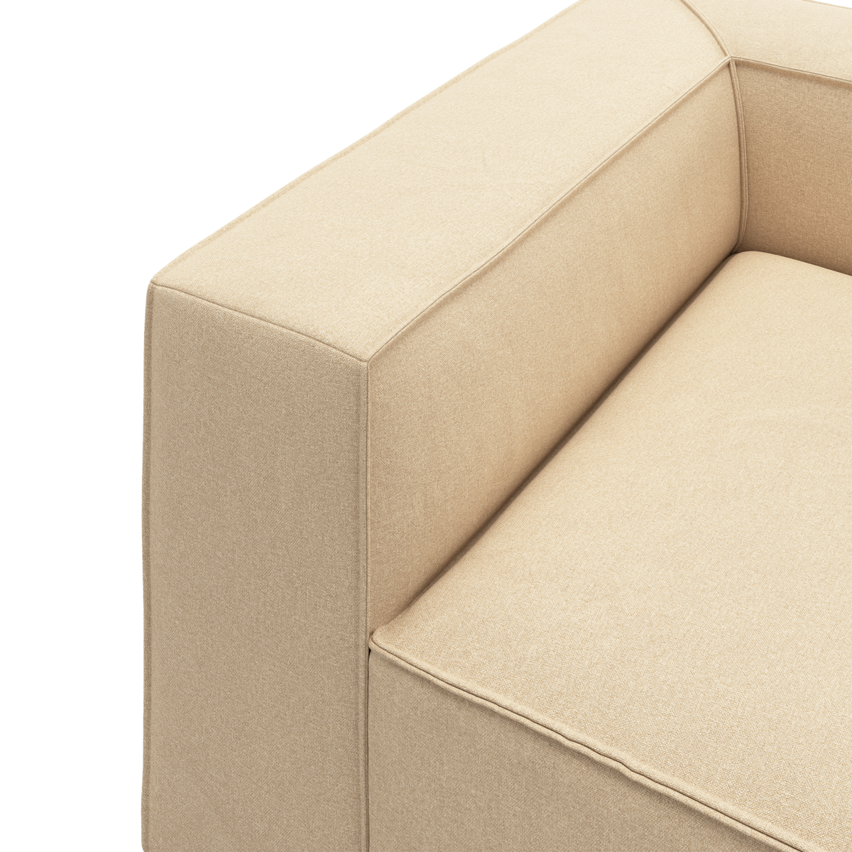 Nærbillede af beige stofsofa med firkantet armlæn og sæde i studiemiljø.