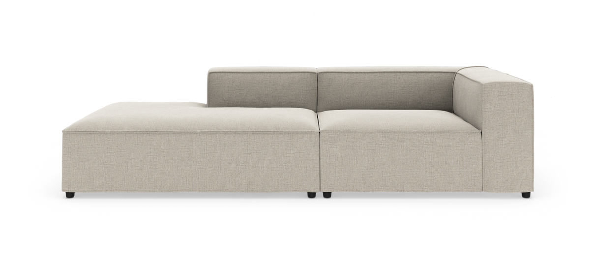 Modulsofa i beige stof med venstre chaiselong og højre armlæn, kubiske former og lav ryg, fritlagt mod hvid baggrund.