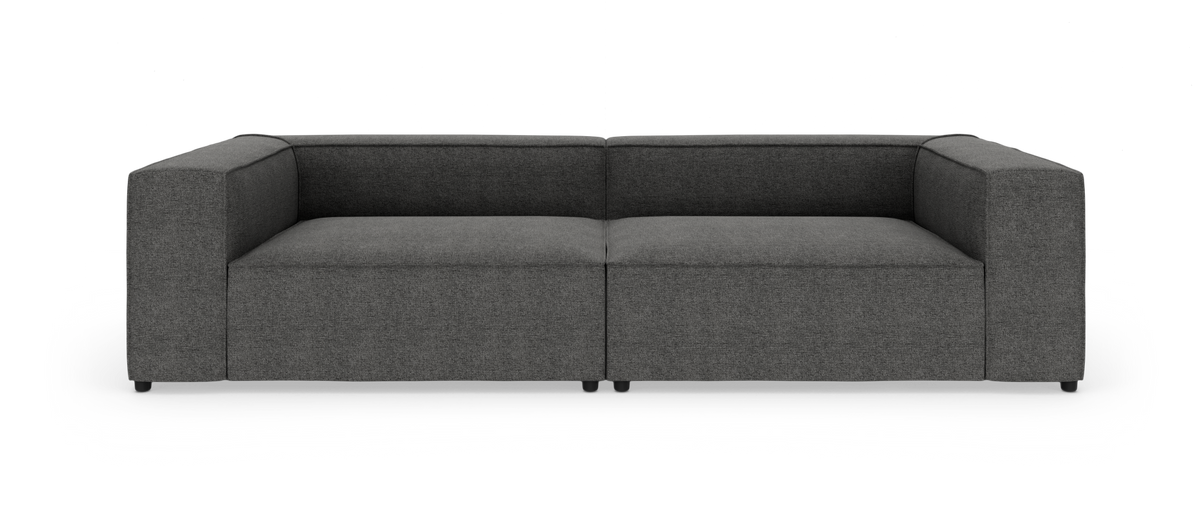 Mørkegrå, lav modulsofa med brede armlæn, fotograferet lige for mod hvid studiobaggrund.