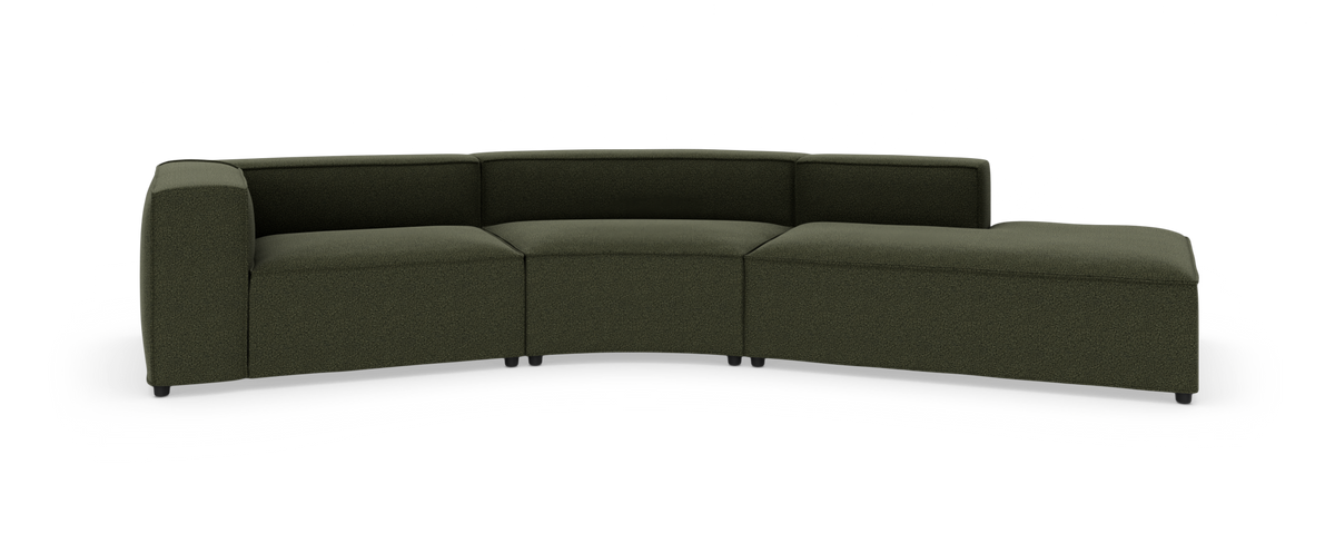 Modulsofa i mørkegrønt stof, let buet med lav ryg og chaiselong i højre side, fritstående på hvid studiebaggrund.