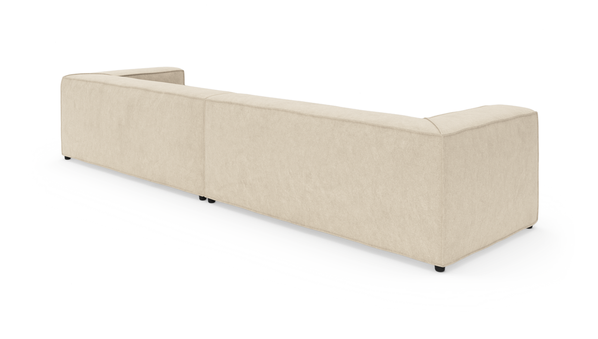 Beige modulsofa set bagfra i studiomiljø, bred L‑form, frilagt på hvid baggrund.