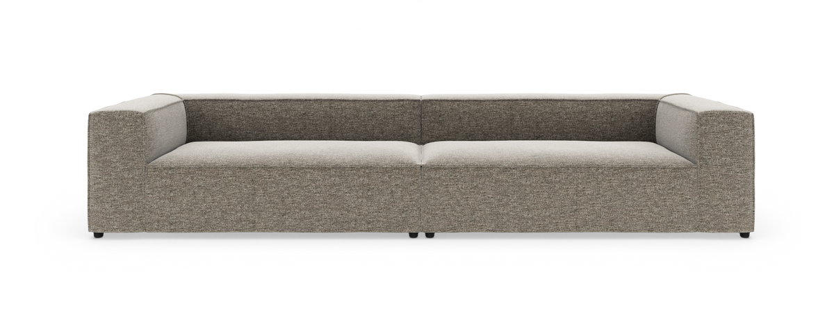 Moderne lav modulsofa i grå/beige stof med brede armlæn, set forfra på hvid baggrund.