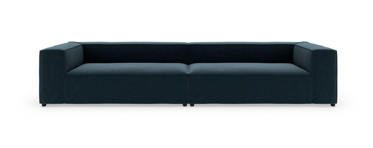 Mørkeblå modulsofa med lav ryg og firkantede armlæn, fotograferet lige forfra i studie på hvid baggrund.