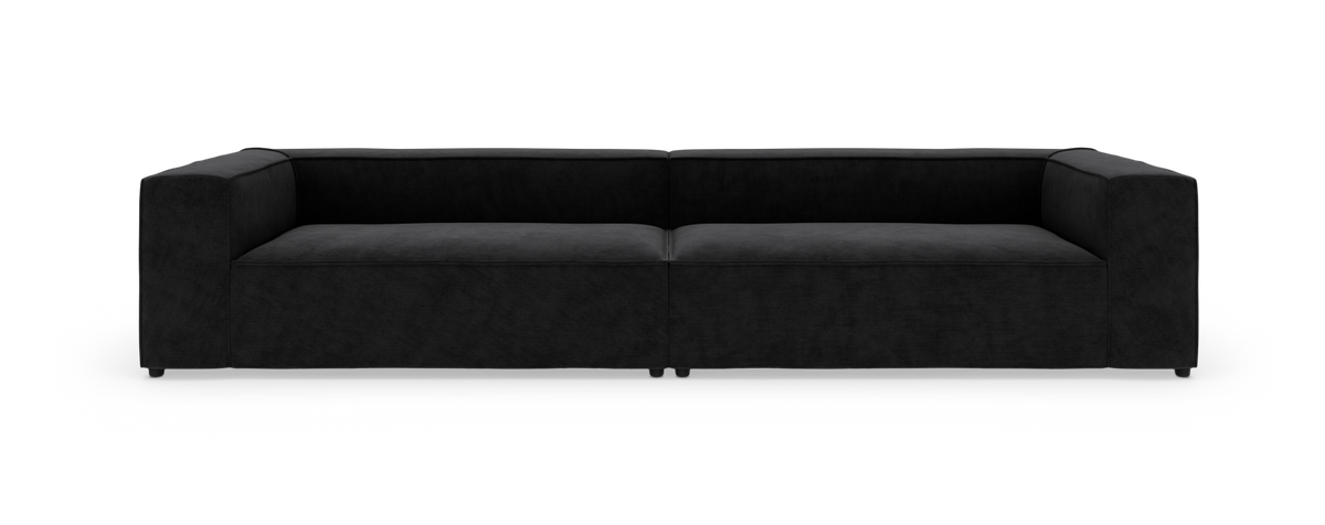 Sort modulsofa med bred, lav siddehøjde og rette armlæn, fotograferet forfra mod hvid baggrund.