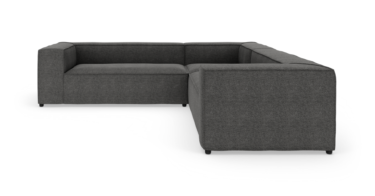 Mørkegrå L-formet modulsofa i stof på hvid studiobaggrund, set i frontvinkel.