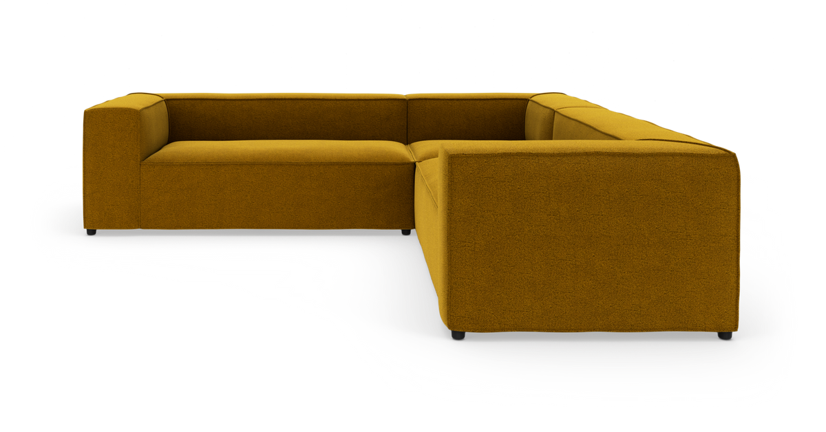 L‑formet modulsofa i sennepsgul tekstil med lav ryg og brede, lige armlæn, fritstående på hvid studiebaggrund.