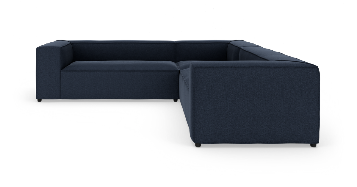 Mørkeblå L‑formet modulsofa i tekstil på hvid studiobaggrund.