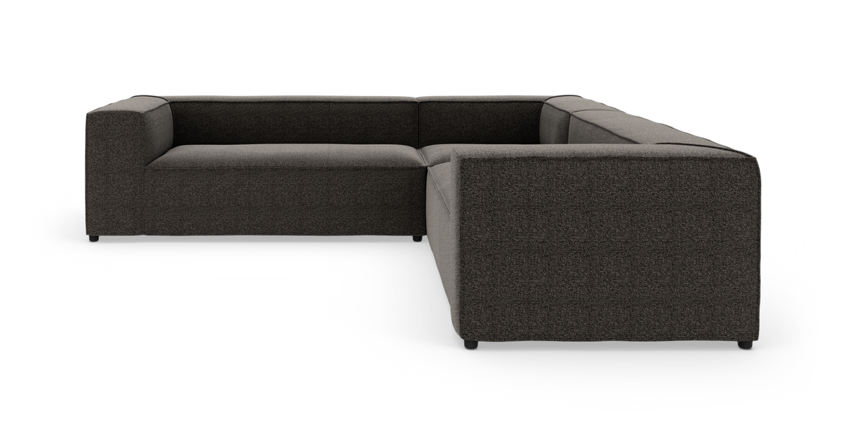 Modulær L-formet sofa i mørkegråt stof på hvid baggrund, vist i studieopstilling.
