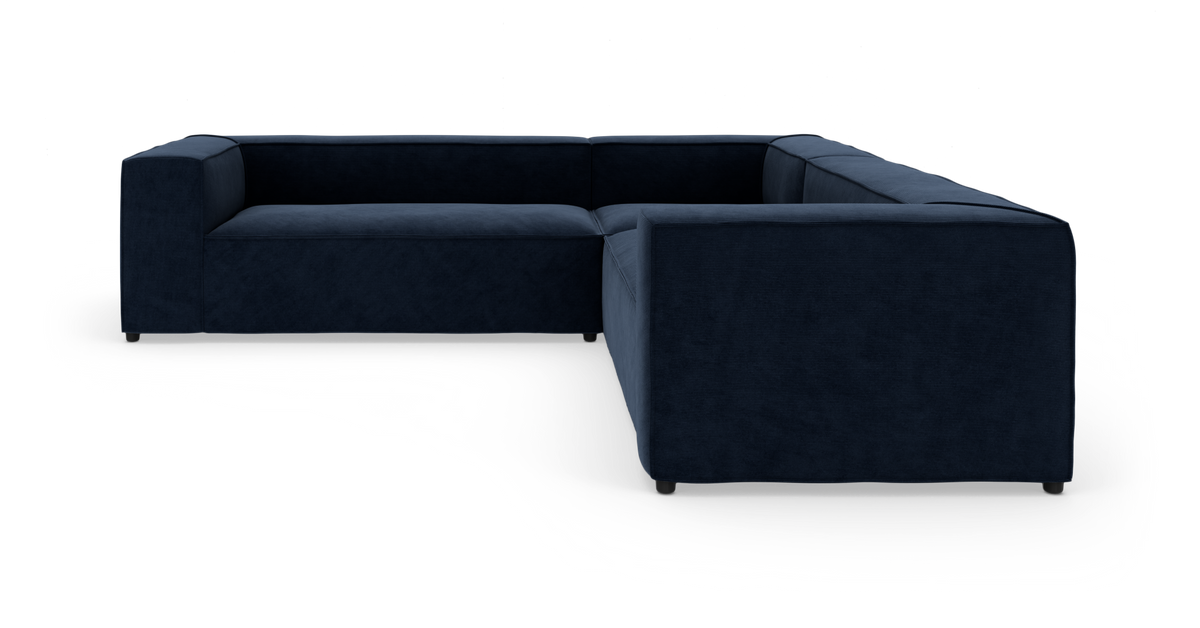 Mørkeblå L‑formet modulsofa med brede lave armlæn og bløde sæder på hvid studiobaggrund, moderne og minimalistisk.