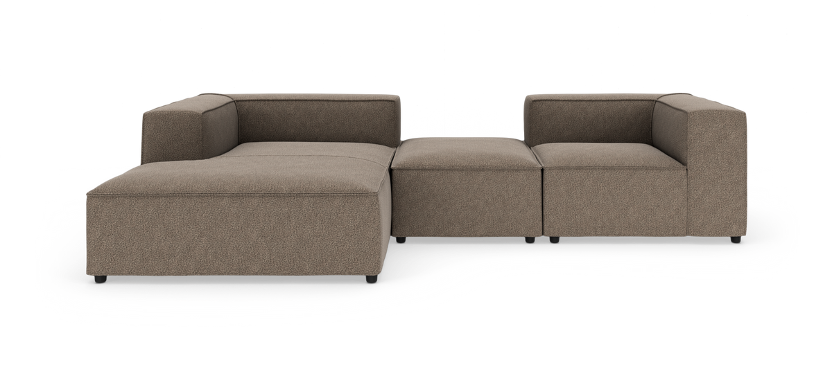 Modulsofa i brun‑beige stof med lav profil og kubiske armlæn, fotograferet mod hvid studiebaggrund.