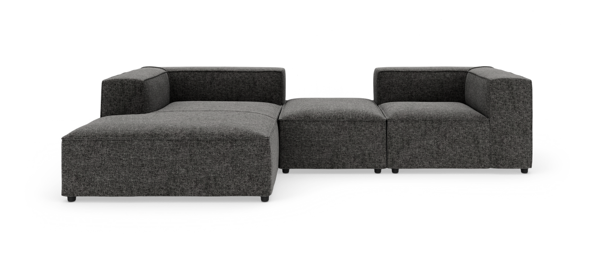 Mørkegrå modulsofa i tekstil med lav profil og kubeformede armlæn på hvid studiebaggrund.