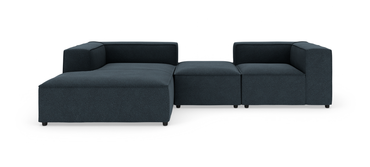Modulær mørkeblå stofsofa med chaiselong til venstre og åbent hjørne, fritstående på hvid baggrund.