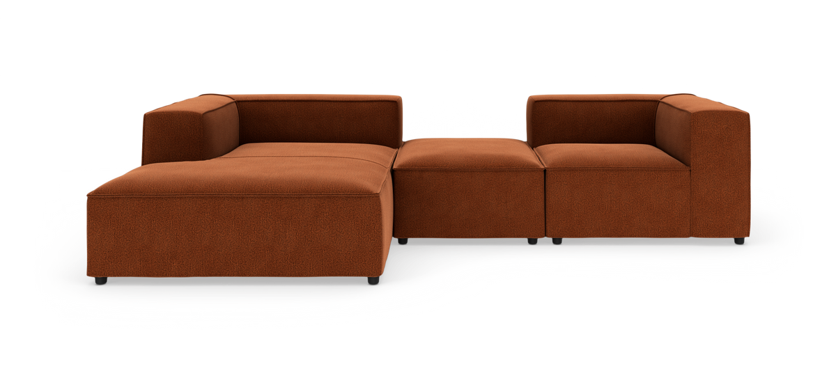Rustbrun modulsofa i stof i L-form med lav ryg og brede armlæn, fotograferet lige for i studiemiljø på hvid baggrund.