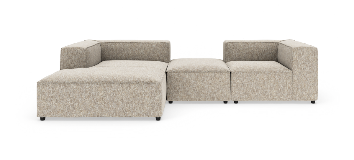 Modulsofa i beige stof med lav ryg og bred chaiselong, frilagt på hvid baggrund.