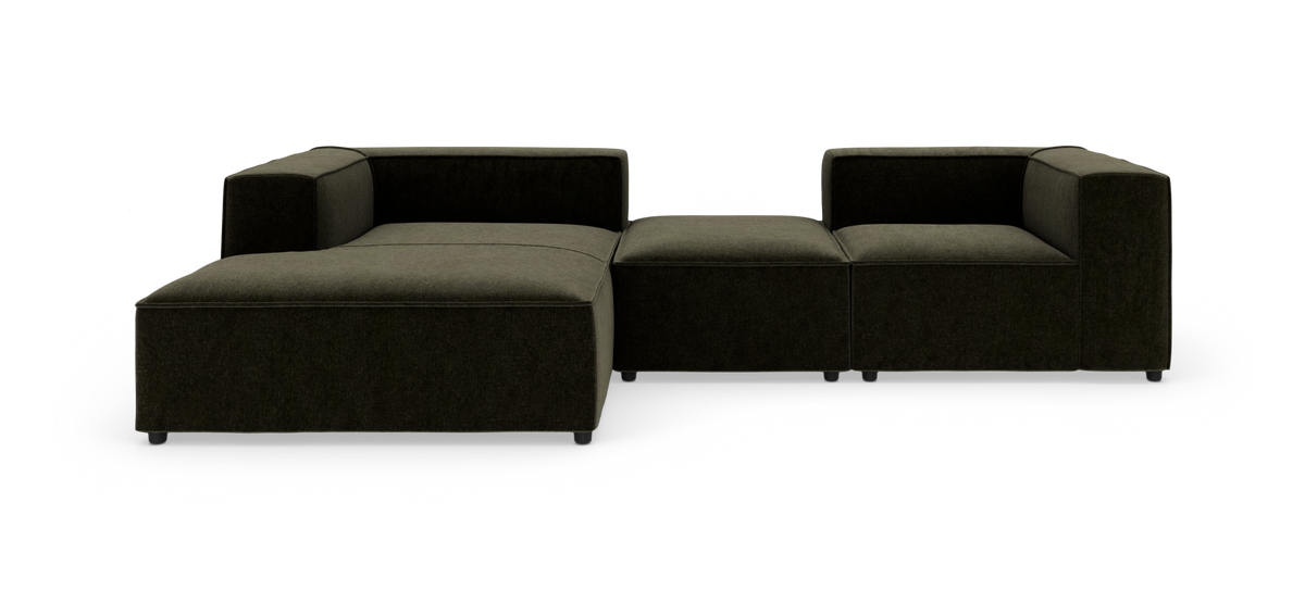 Modulsofa i mørk olivengrøn tekstil, lav og boxet med bred chaiselong til venstre og åben midtermodul, vist i frontvinkel.