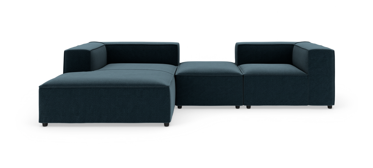 Modulsofa i mørk petrolblåt stof med venstrevendt chaiselong og brede lave armlæn, fritlagt på hvid baggrund.