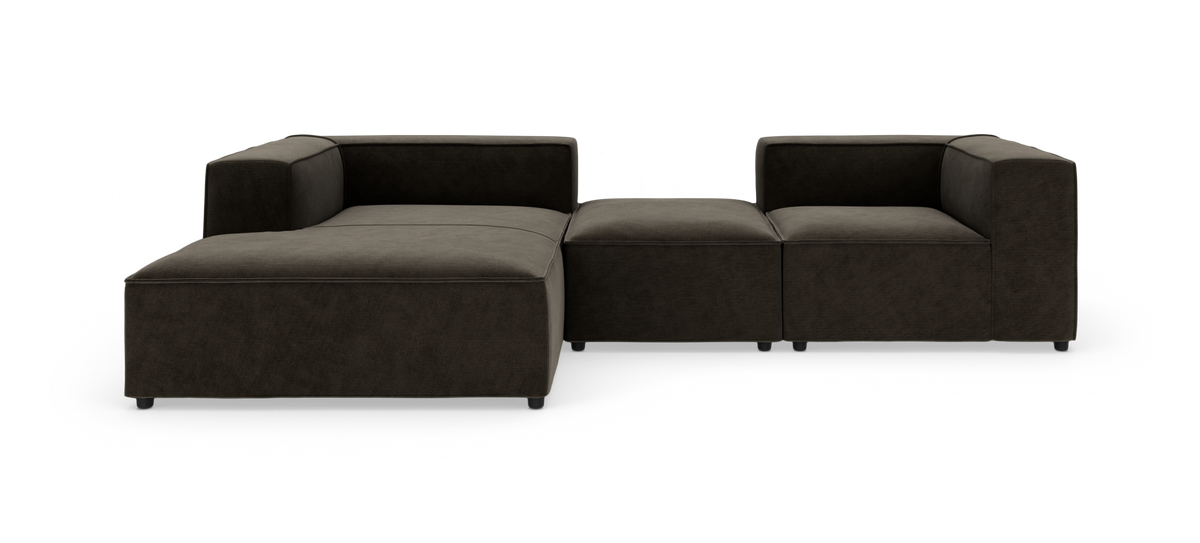 Modulær mørkebrun hjørnesofa med bred chaiselong og midterpuf, vist forfra på hvid studiobaggrund.
