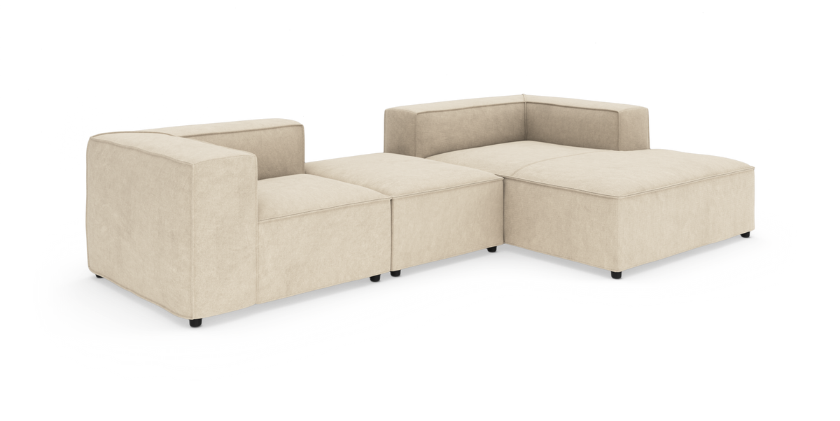Beige modulsofa i stof – lav L‑formet hjørnesofa med bred chaiselong, frilagt på hvid baggrund.