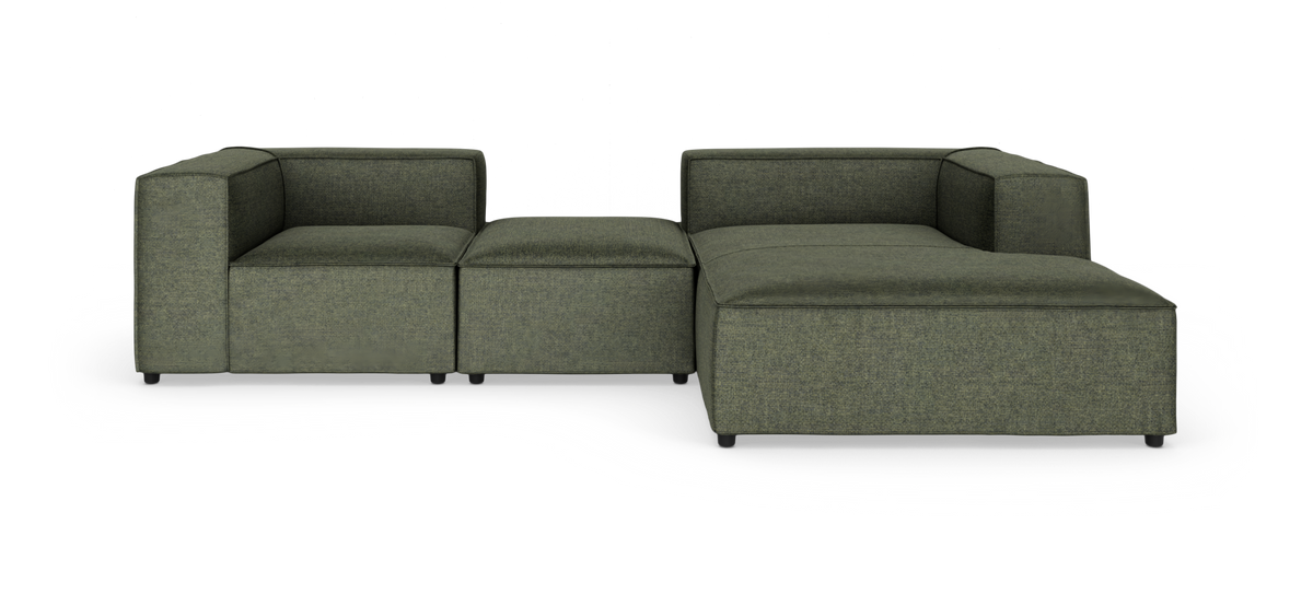 Modulsofa i mørkegrønt stof, L‑form med bred chaiselong, isoleret på hvid baggrund.