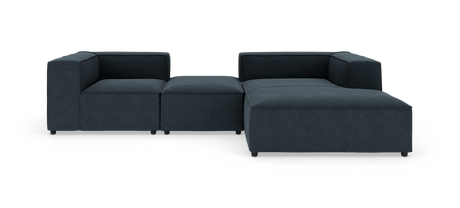 Modulsofa i mørkblåt stof, L‑form med lav ryg og bred chaiselong på hvid studiobaggrund.