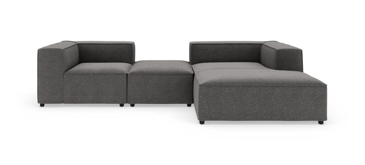 Modulsofa i mørkegråt stof med chaiselong og puff, kubiske armlæn, frilagt på hvid baggrund.