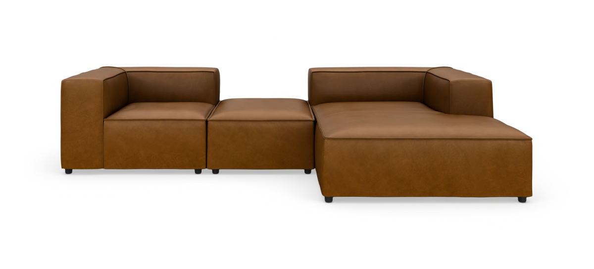 Brun modulsofa i læder med chaiselong til højre, lave kubiske armlæn og bred siddeflade, frilagt på hvid baggrund.