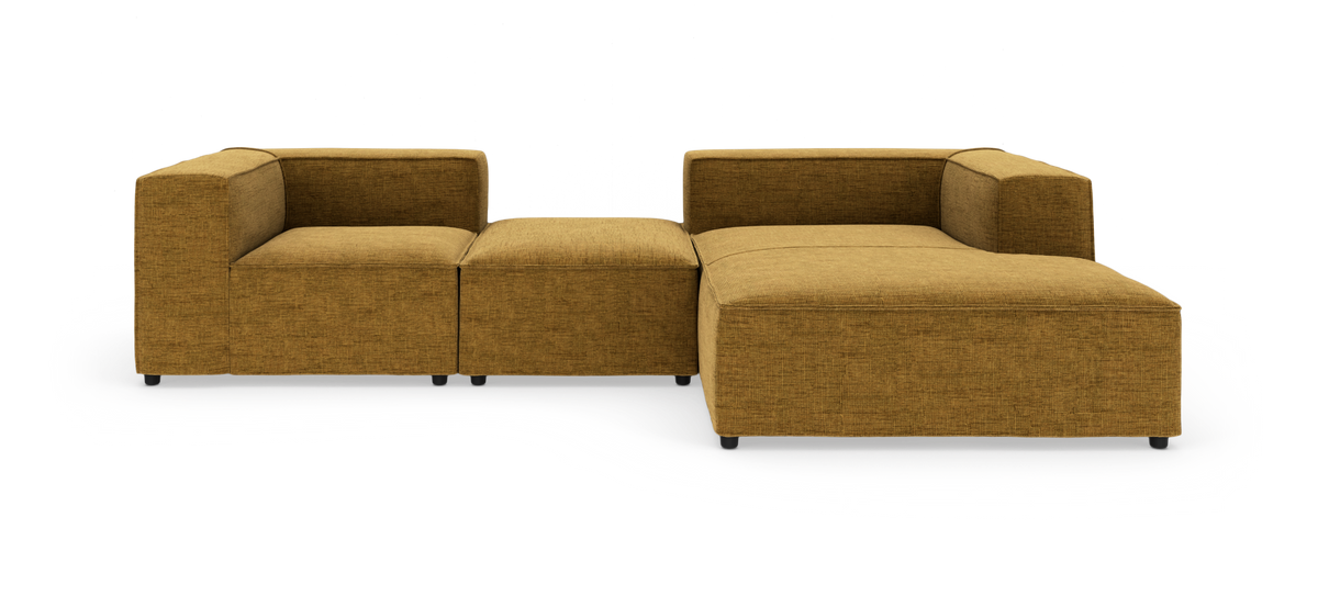 Modulær sennepsgul stofsofa i L‑form med brede armlæn og en ottoman, frilagt på hvid baggrund i frontvisning.
