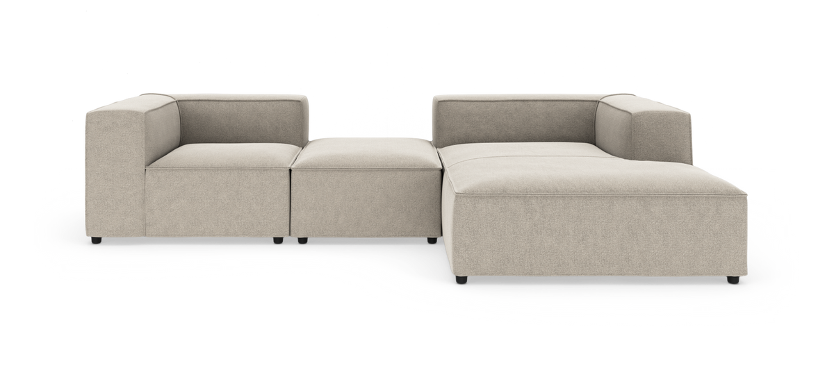 Beige modulsofa i L-form med chaiselong til højre, bokseformede armlæn og lave sorte ben på hvid studiebaggrund.
