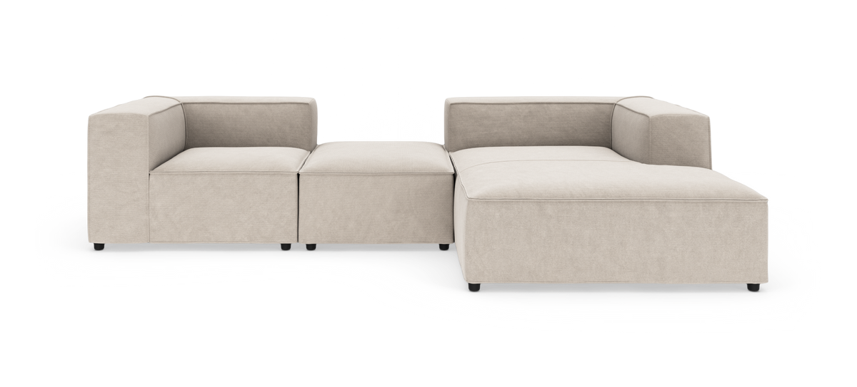 Modulær L‑sofa i beige stof med brede, kantede armlæn og lav profil, fritlagt på hvid baggrund.