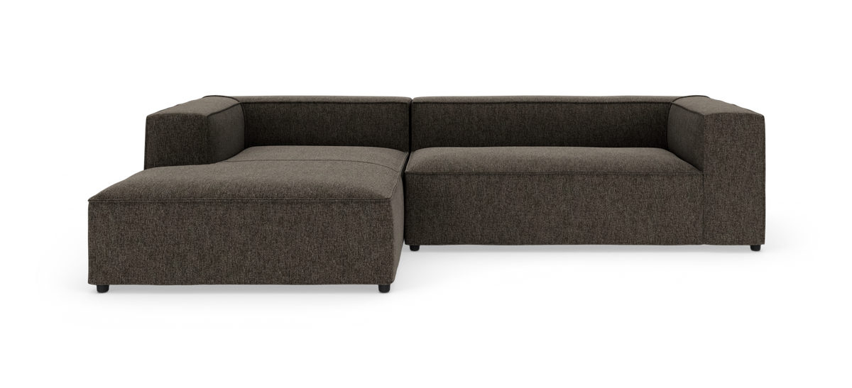 Modulær L-sofa i mørkgrå/brun meleret tekstil med venstrevendt chaiselong og lave, lige armlæn; frilagt på hvid baggrund.