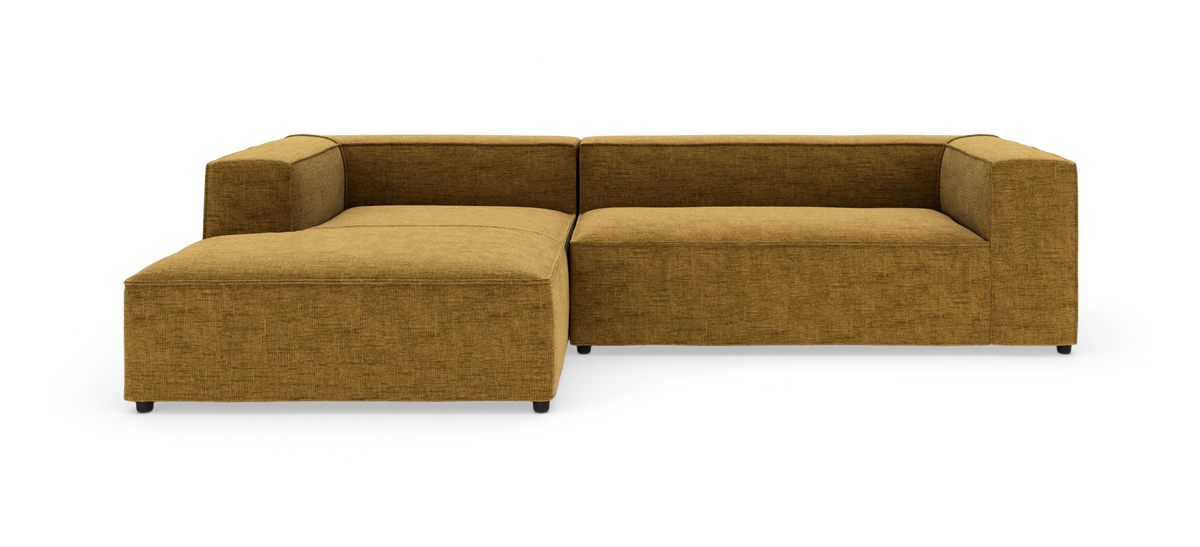 Modulsofa i L-form med bred chaiselong til venstre, polstret i sennepsgul tekstil, frilagt mod hvid baggrund.