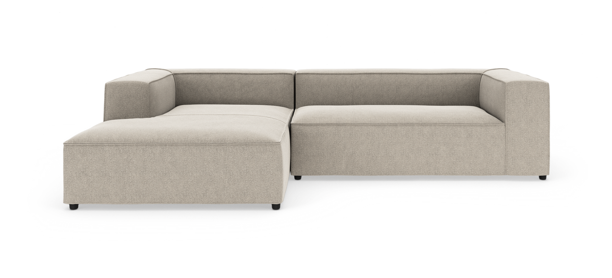 L‑formet modulsofa i beige stof med lav profil og bred chaiselong til venstre.