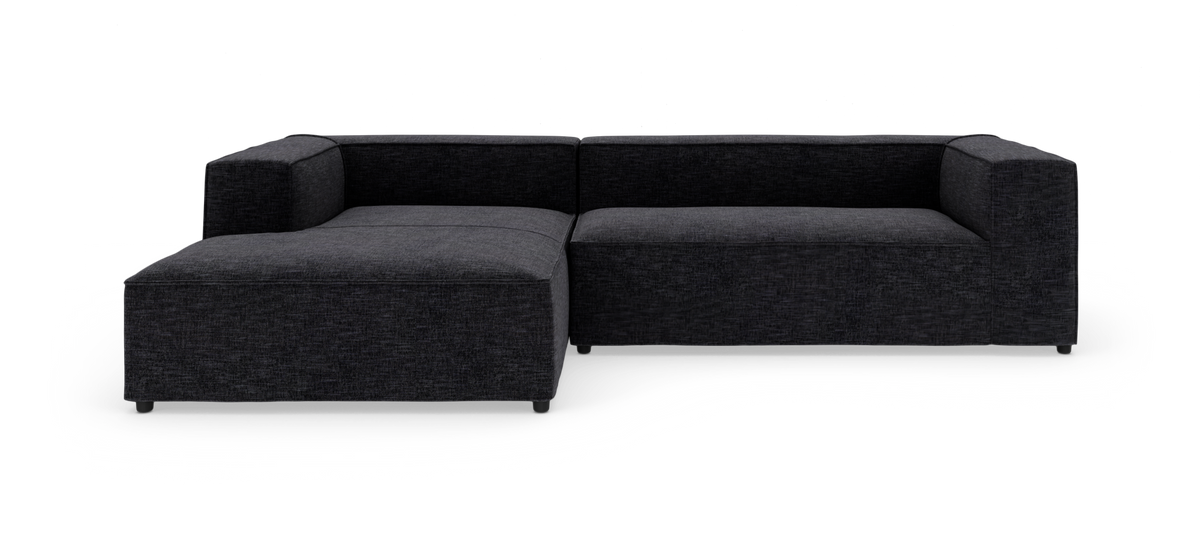 Mørkegrå L-formet modulsofa med chaiselong til venstre, fotograferet mod hvid baggrund.