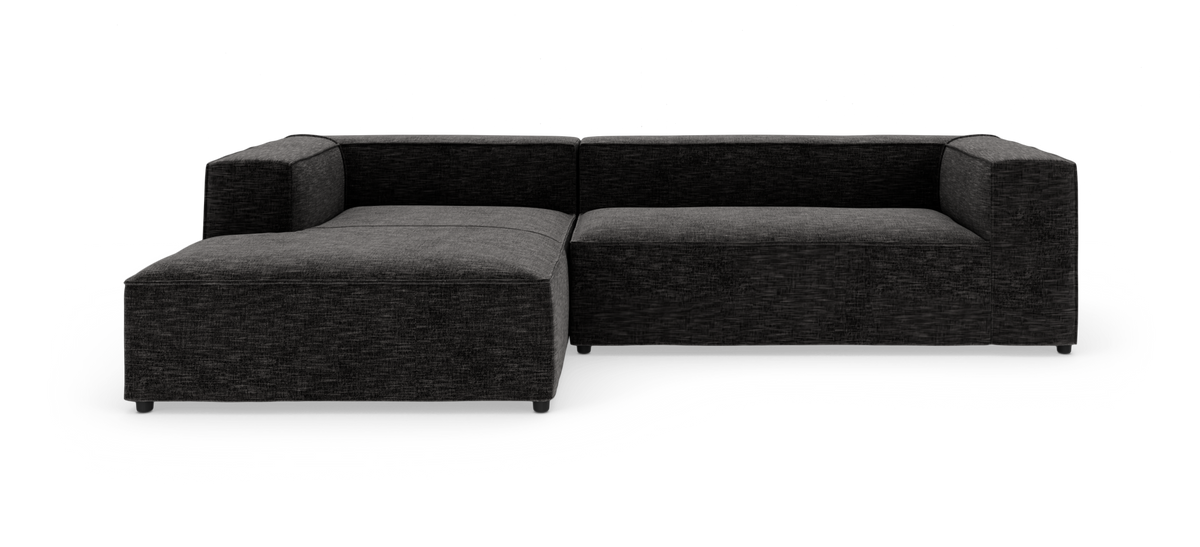 Mørkegrå modulsofa i L‑form med venstre chaiselong, frilagt på hvid baggrund.