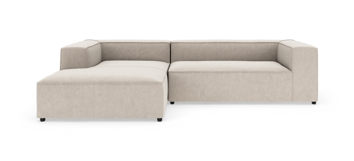 Beige L-formet modulsofa med bred chaiselong, tykke hynder og rette armlæn på hvid baggrund.