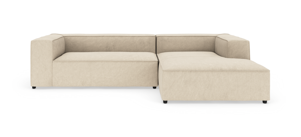 Beige modulsofa i L-form med bred chaiselong til højre.